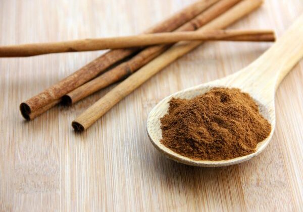 A spoonful of cinnamon and cinnamon sticks set on a bamboo wooden surface